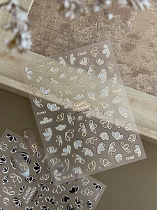 Détail de stickers à ongles dorés et argentés avec motifs floraux et papillons