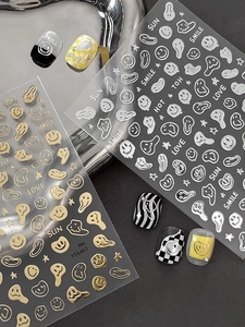 Close-up of gold and silver melting smiley face nail art decals with letter motifs