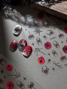 Close-up of gothic spider and web nail stickers with red gem accents on display tips
