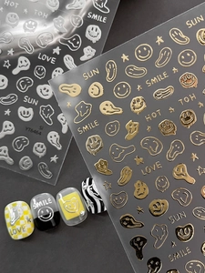 Macro detail of 3D embossed gold and silver smile face nail art decals on dark base