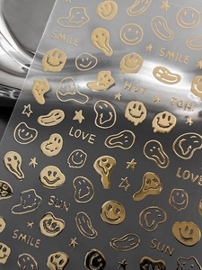 Close-up of gold embossed smiley face nail stickers with 3D metallic texture details