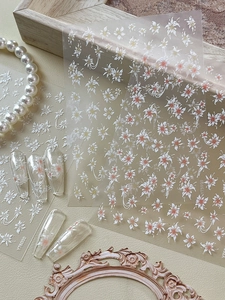 Vue macro de stickers ongles fleurs en relief 3D avec textures florales blanches et oranges