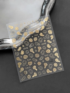 Detail of gold metallic nail art stickers with smiles and stars on a clear sheet