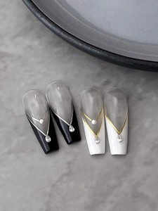 Detail of long coffin nails with black and white V-shape French lines, pearls, and rhinestones