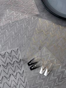 Close-up of minimalist V-shape geometric nail stickers in gold, silver, and black finishes