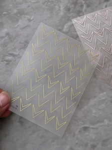Close-up of gold and rose gold chevron nail stickers with metallic finish on gray stone