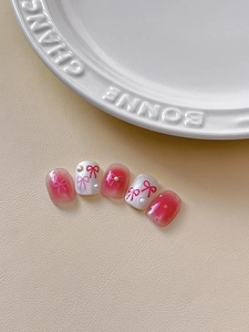Detailed close-up of pink bow press-on nails with tiny pearls and gradient patterns