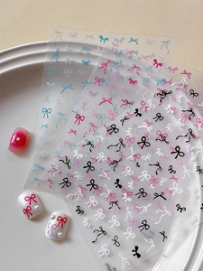 Detailed view of colorful bow nail stickers on white ceramic plate with pearls