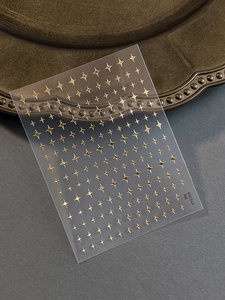Detailed view of golden starburst nail art stickers on a matte semi-transparent sheet