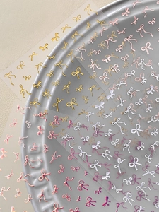 Macro shot of 3D bow nail stickers with gold and pearl pink metallic embossed details