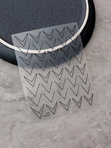 Macro detail of black V-shaped French line nail art stickers on a grey marble background