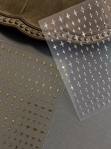 Macro shot of gold and silver four-pointed star nail stickers with metallic gloss finish