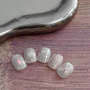Y2K style press-on nails with rose gold kitty and bow motifs on pearl white base