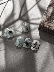 Dettaglio di nail art Halloween cat-eye con ragni neri e ciondoli a croce in argento lucido