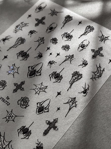 Dettaglio macro di adesivi goth per unghie di Halloween con ragni neri e croci decorativi