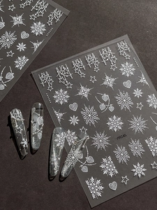 Detail of white embossed snowflake and star nail art stickers on a dark matte background