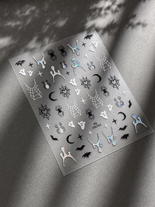 Detail showing Halloween nail stickers with spiders and ghosts on textured dark background