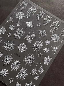 Macro shot of 5D white embossed Christmas nail stickers with snowflakes and stars on grey background