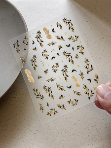Dettaglio di adesivi per unghie stile cinese con fiori di osmanto e calligrafia dorata