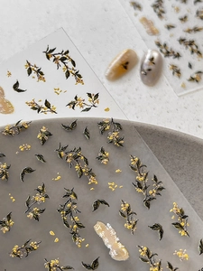 Dettaglio di adesivi per unghie osmanto con fiori gialli in rilievo e lamina d'oro