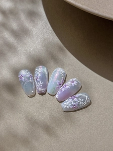 Dettaglio di unghie finte sfumate lavanda con nail art 3D e decorazioni di perle