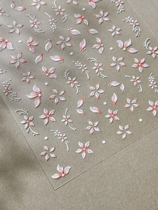 Vista macro di adesivi 3D per unghie con petali di fiori bianchi e rosa in rilievo