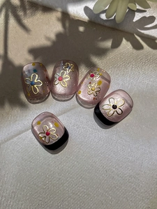 Detailed macro view of gold flower nail stickers on translucent pink glitter press-on nails