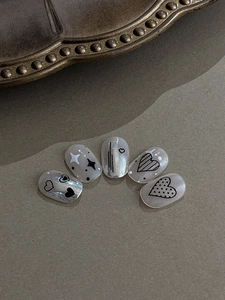 Macro detail of silver pearl nails featuring hand-painted hearts and star motifs