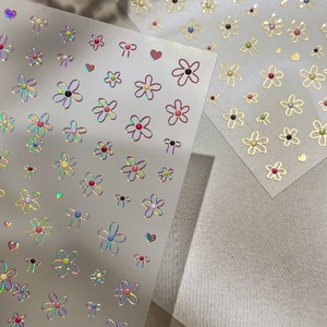 Holographic and gold floral nail stickers with heart and bow designs on beige fabric