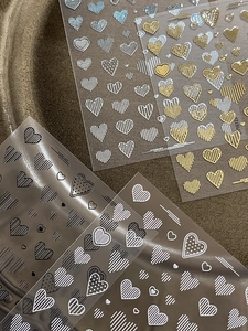 Detailed view of heart pattern nail stickers in gold, silver, black, and white colors