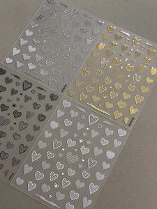 Detail of embossed heart nail stickers in gold, silver, black, and white finishes