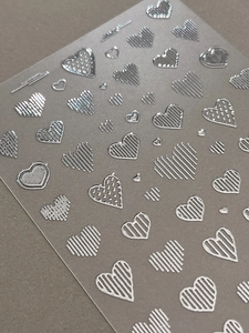 Macro shot of silver 3D embossed heart nail stickers with metallic relief textures