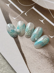 Detail of light blue and white oval nail stickers with floral patterns and pearl accents