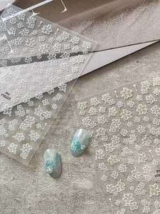 Detailed view of white floral nail art stickers with pearl accents on teal nails