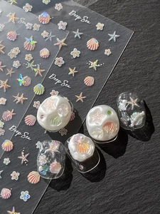 Makroaufnahme von 3D-Nagelstickern mit Muscheln und Seesternen mit Aurora-Glitzereffekt