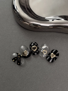 Close-up of handmade press-on nails with heart charms and black checkerboard patterns
