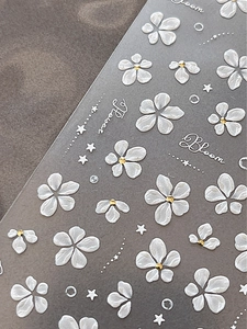 Close-up of 5D white floral nail stickers with golden dots and elegant lettering