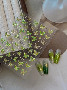 Close-up of gold butterfly nail stickers with star accents and green glitter details
