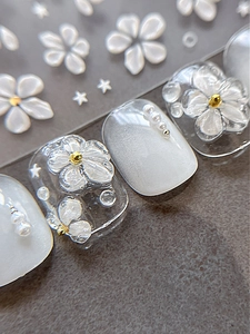 Macro detail of 3D white floral nail art decals with gold beads and pearls accents