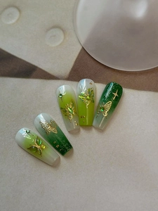 Close-up of green gradient press-on nails with golden butterflies and glitter stars