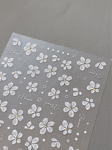 Detail of 3D embossed nail art stickers with white floral patterns and gold accents