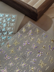 Close-up of gold embossed butterfly nail art stickers with laser purple and starry patterns