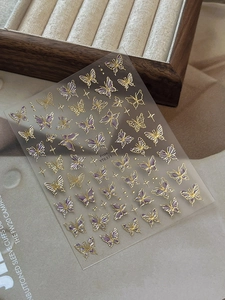 Macro detail of gold foil butterfly nail art stickers with purple gradient accents