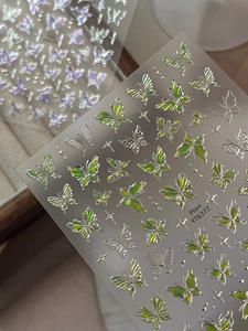 Macro shot of iridescent emerald butterfly nail art stickers with sparkling star accents