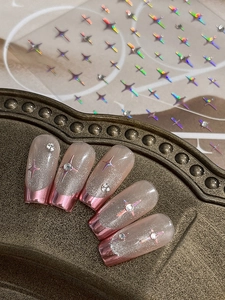Macro detail of nude French nails with pink metallic tips and sparkling star charms