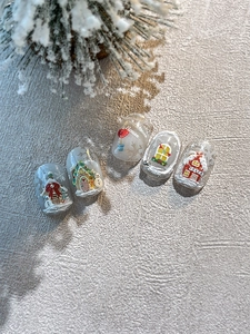 Close-up of 3D embossed Christmas nail charms featuring snowman and snow cabin designs