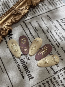 Detailed macro view of matte beige and red press-on nails with gold sun and moon motifs