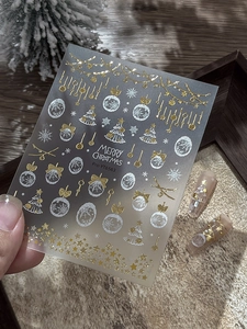 Close-up of gold and white 3D Christmas snowflake nail stickers with festive tree patterns