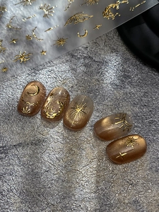 Macro shot of gold 3D embossed sun and moon nail decals on brown cat-eye nails