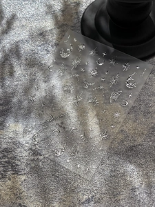 Detailed macro view of 3D metallic moon, stars, and butterfly nail art stickers